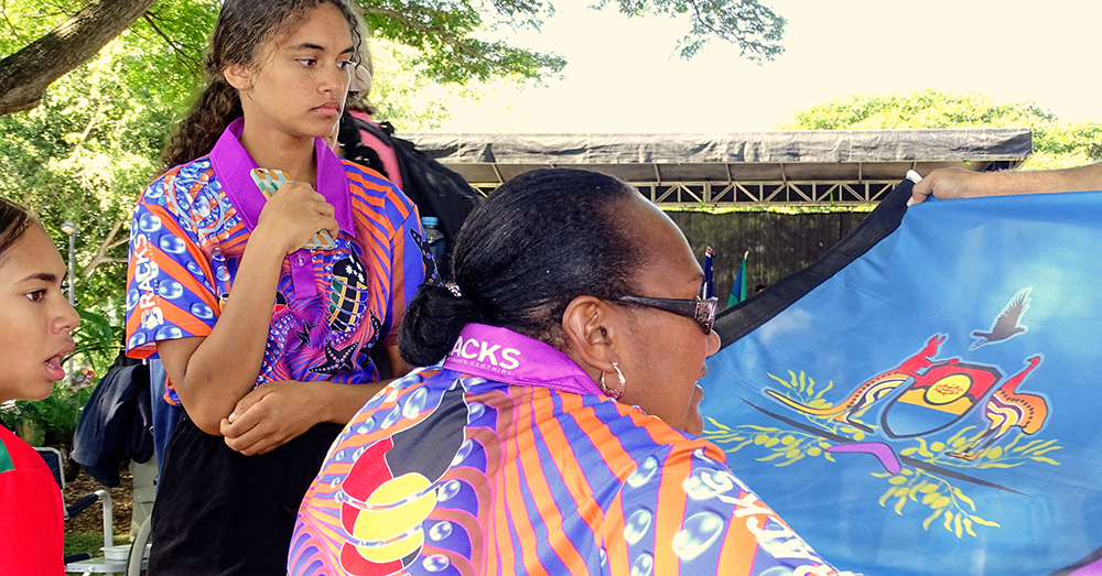 close up of Australian Aboriginal woman and two young Aboriginal women looking at Aboriginal flag.